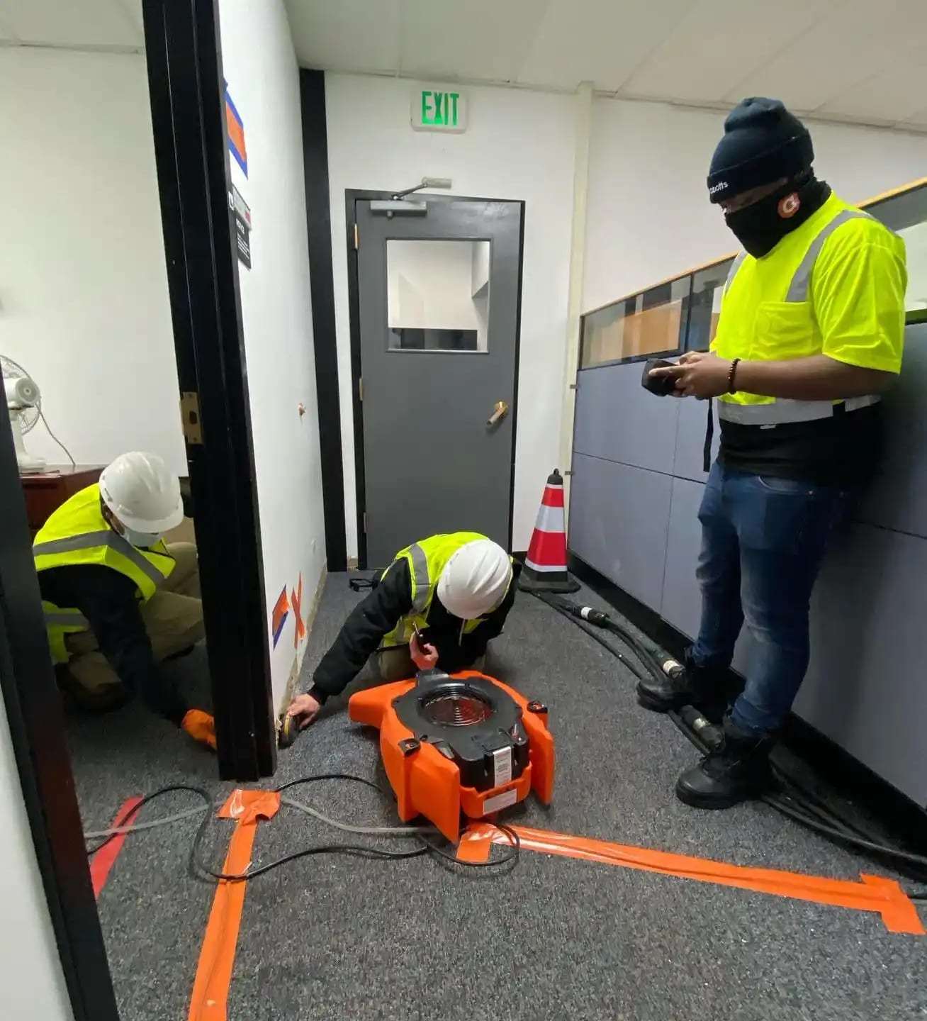 Workers in high-visibility vests setting floor drying equipment in an office